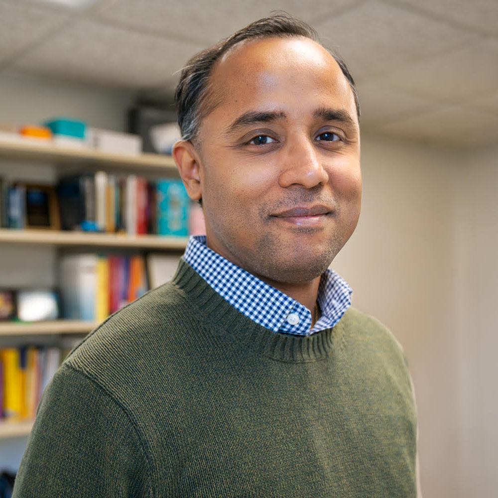 Picture of krishna venkatasubramanian in a check button-down shirt. URI quad in the background.